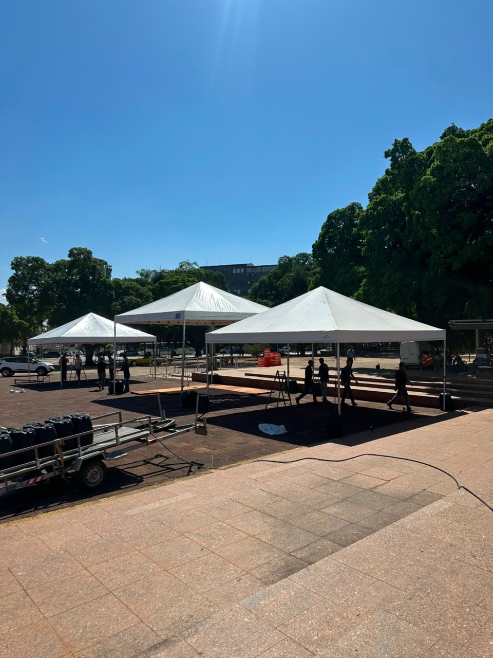Três tendas piramidais brancas montadas lado a lado em uma praça para um evento